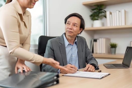 A businessman reviews and signs documents while discussing with a colleague, emphasizing collaboration and attention to detail.