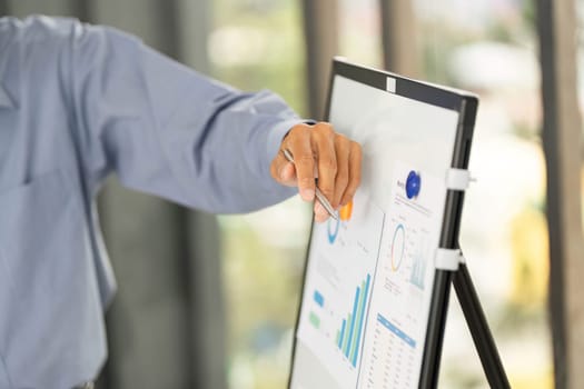 A businessman points at a digital board displaying graphs and charts, emphasizing data analysis in a corporate setting.