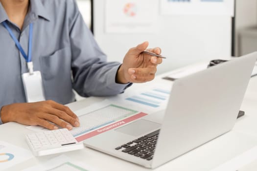 A business professional engaged in remote work, reviewing data on a laptop while holding a pen and documents, showcasing productivity.