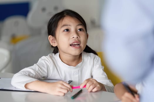 A curious young girl listens attentively in class, showcasing engagement and enthusiasm for learning in a vibrant educational environment.