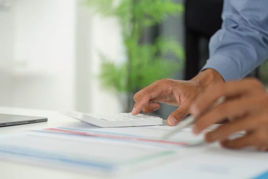 A professional's hand operates a calculator, analyzing reports and data on a modern office desk.