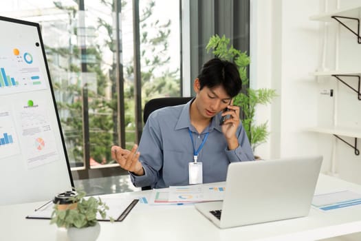 A young man reviewing financial charts and discussing insights over the phone in a bright, modern office space.