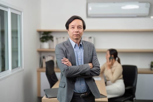 A confident businessman poses in a modern office, demonstrating leadership qualities while a colleague works in the background.