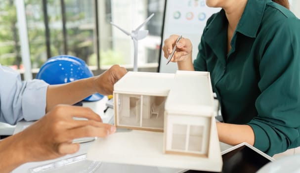 Engineers analyze a miniature house model, focusing on sustainable design and renewable energy solutions in a collaborative workspace.
