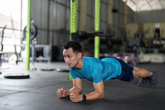 A focused man engages in a plank exercise, showcasing strength and determination in a well-equipped gym setting.