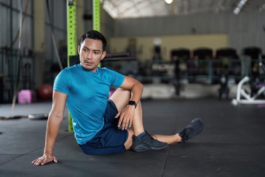 A young man sits on the gym floor, preparing for a stretching routine that enhances flexibility and promotes recovery.