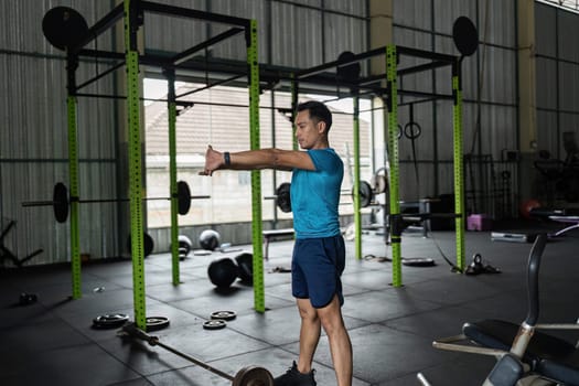 A fit male prepares for his workout by stretching his arms in a gym, emphasizing the importance of warm-up.