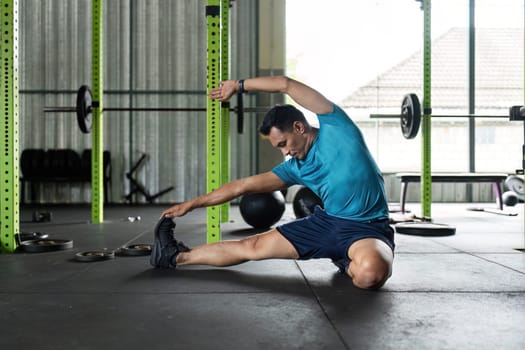A fit man performs a side stretch in a gym, focusing on flexibility and wellness. Ideal for health and fitness themes.