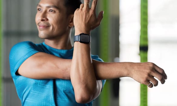 A man performs an arm stretch in a gym, emphasizing the significance of flexibility and warm-up exercises in fitness.