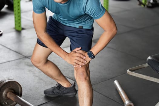 A man in a gym setting holds his knee in discomfort, highlighting the importance of injury prevention in fitness routines.