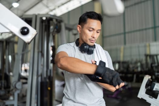 A focused man in a gym setting adjusts his workout gloves and headphones, ready for an intense training session.