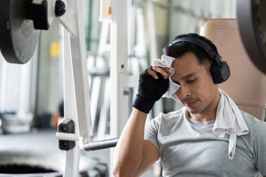A determined man wipes sweat from his forehead, reflecting resilience and focus during an intense gym session.
