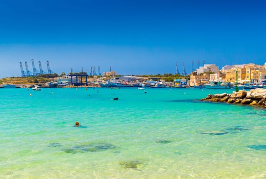 A beautiful view of the small Maltese town of Marsaxlokk with turquoise clear sea water and the port in the background.