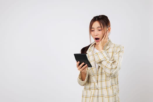 Holding a calculator tightly, woman shows a shocked reaction while checking the calculator again, facing accounting confusion and financial concerns. isolated studio white background, Tax day concept
