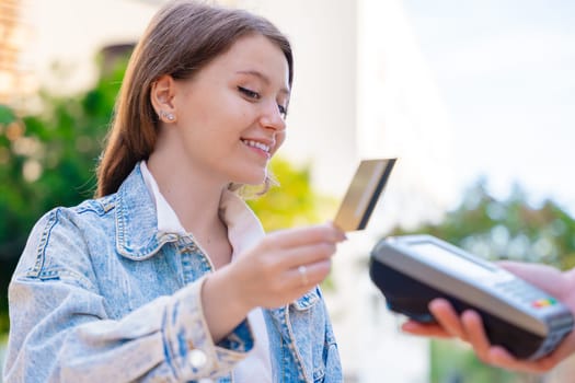 Caucasian woman smiling as she pays with a credit card using contactless technology at an outdoor cafe. A casual urban moment reflecting convenience, lifestyle, and modern financial habits.