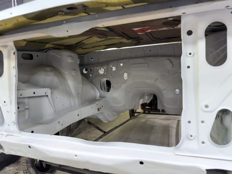 Clean view of stripped car engine bay during the restoration process, showing primed metal surfaces and intricate structural details in preparation for mechanical assembly or repainting