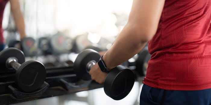 A close-up shot of a man gripping a dumbbell, emphasizing strength training and fitness in a gym environment.