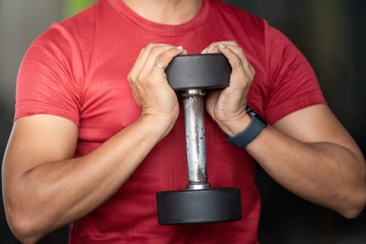 A man holds a dumbbell close to his chest, preparing for a workout in a gym, emphasizing wellness and strength training.