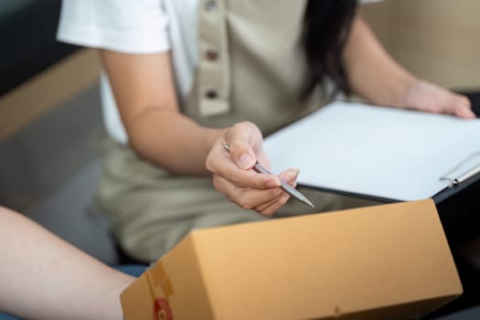 A woman writes on a clipboard while her partner organizes packages, highlighting their collaborative efforts in e-commerce logistics.