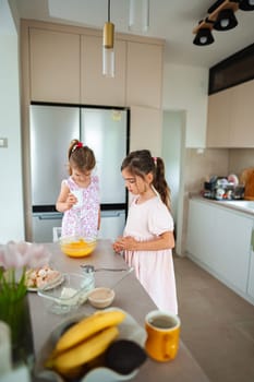 Two young girls enjoy baking together in a cozy kitchen.