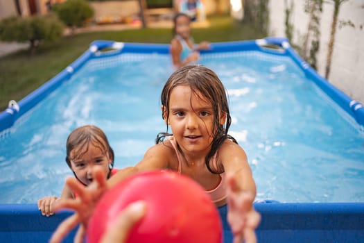 Girls enjoy a sunny day splashing and playing in their backyard pool.