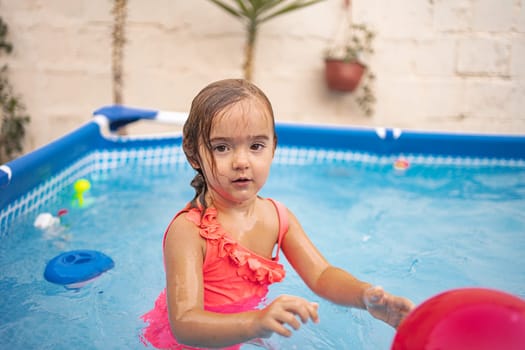A girl splashes in a swimming pool filled with toys on a sunny day.