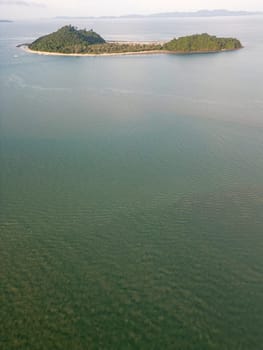 Drone shot of a stunning travel destination featuring crystal clear waters and coastal cliffs, dense forest on a small island in Thailand. Sunlit seashore with sailboats on the coastline.