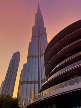 UAE, Dubai, 10 December 2024: The famous Burj Khalifa skyscraper at dusk, Dubai's sights during the incredible sunset sky, skyscrapers illuminated at night, pink sky, palm trees. High quality photo