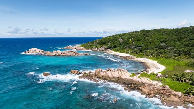 Tropical greenery meets clear turquoise ocean waters, with rocky outcrops along the coastline. La Digue, Seychelles.