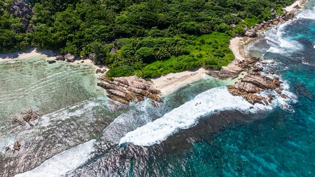 Clear shallow water leading up to a sandy tropical beach with a forest in the background. La Digue, Seychelles.