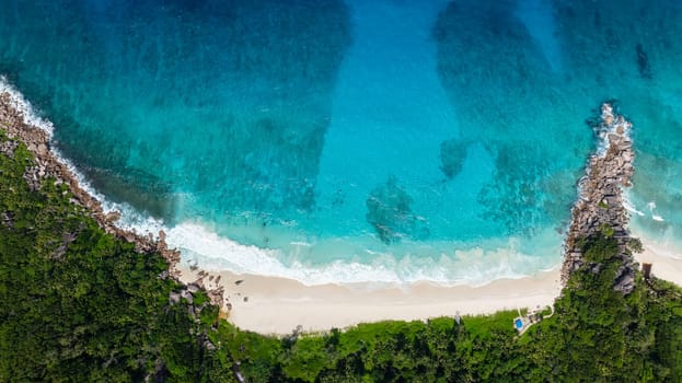 Top view showing a white sandy beach with turquoise water and dense green foliage along the shore. Seychelles, La Digue.