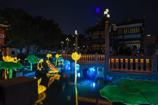 Shanghai, China - 1 April 2025: Lantern-lit lotus flowers and fish float on the pond at night in historic Yuyuan Garden during the spring light festival.