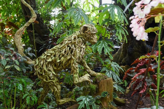 Singapore, Singapore - 4 April 2025: Wooden sculpture of a monkey made from twisted roots on display among lush tropical plants in the Cloud Forest, Gardens by the Bay.