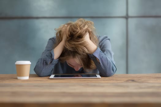 Young professional woman experiencing stress and burnout while working in a modern office, covering her face with hands and struggling with a difficult task or deadline..