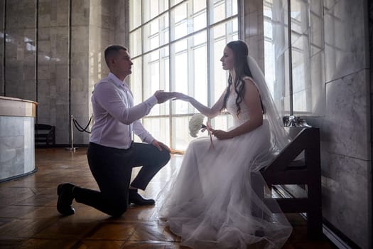 Groom kneels before bride, expressing love and commitment during wedding registration in a beautifully lit venue.