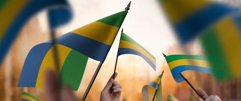Gabon flags in their hands on a blurred urban background. The photo illustration was created without the use of artificial intelligence, only using Photoshop.