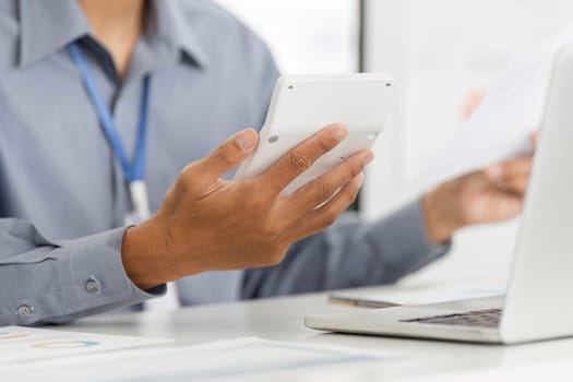 A professional in a remote work setting, using a calculator while holding documents, highlighting analytical skills and productivity.