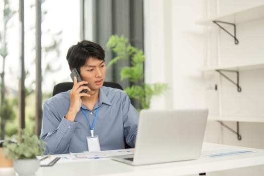 A young man engaged in a phone call while reviewing paperwork in a home office, showcasing remote work professionalism and focus.