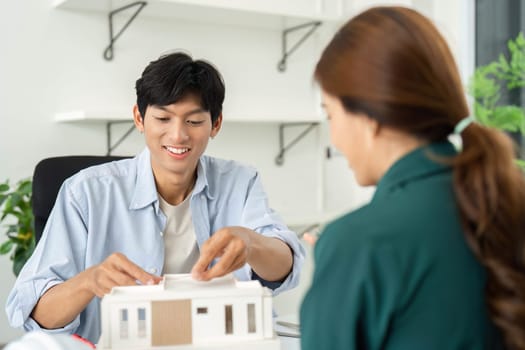 A young woman and man discuss a sustainable architectural model, showcasing collaboration and innovation in a bright office environment.