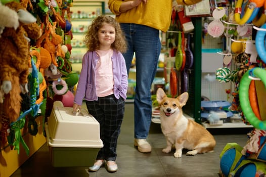 Portrait of little girl child standing with new carrier for corgi dog posing for camera among pet shop showcase. Happy family shopping at vet store