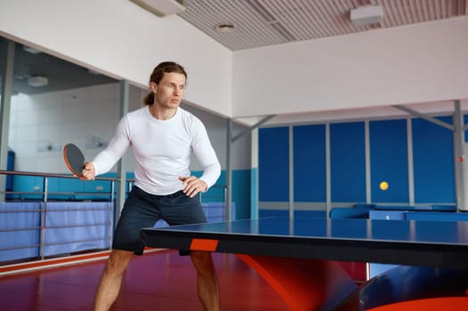 Portrait of young table tennis player training in sport club. Hipster guy enjoying ping pong game practicing technique