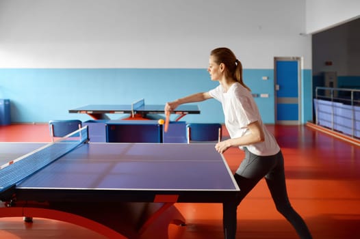 Young woman kicking ball playing table tennis at sport club. Female practicing ping pong before competition event