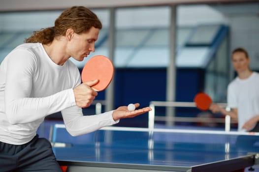 Man and woman playing table tennis, focus on sportsman player serving ball with racket. Sport and healthy lifestyle concept