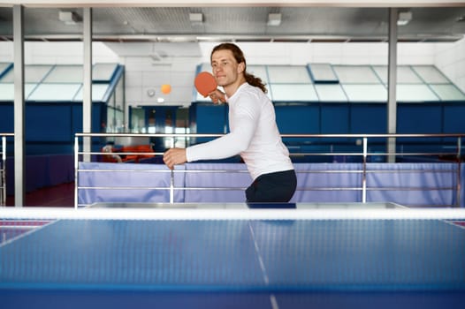 Portrait of young table tennis player training in sport club. Hipster guy enjoying ping pong game practicing technique