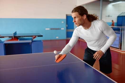 Young man table tennis player kicking ball with racket in motion. Professional sport and active lifestyle concept