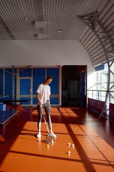 Young woman cleaning floor picking balls after training class or competition at modern ping pong sport club