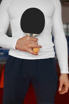 Cropped shot of table tennis racket and ball in male hand. Ping pong training class, sport completion and championship concept