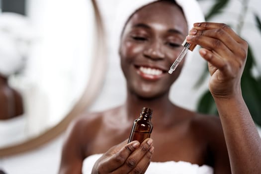 A woman enjoys her skincare routine at home, holding a dropper bottle filled with serum. She smiles brightly while applying the serum, surrounded by a serene atmosphere.