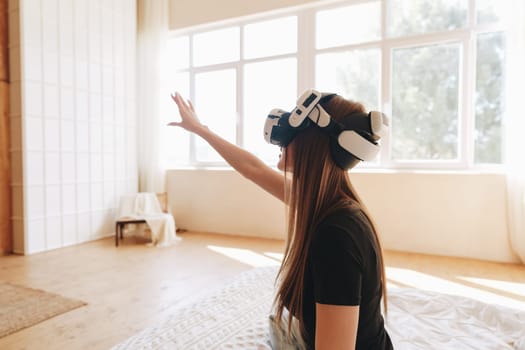 A person wearing a virtual reality headset gestures in a well-lit room filled with natural light.
