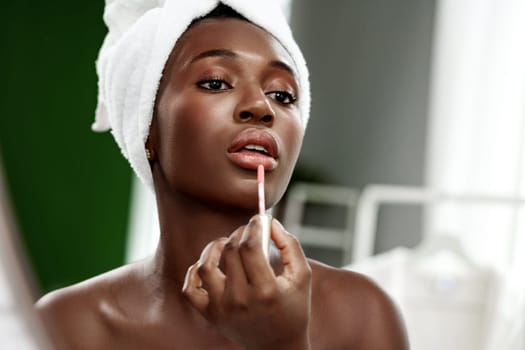 A woman focuses on applying lip gloss in a stylish, well-lit environment. The calming atmosphere highlights her beauty routine in a cozy home setting.